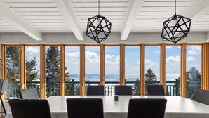 Une table de conférence avec quatre chaises, de grandes fenêtres donnant sur l’océan et des luminaires suspendus aux formes géométriques.