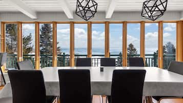 Une table de conférence avec quatre chaises, de grandes fenêtres donnant sur l’océan et des luminaires suspendus aux formes géométriques.