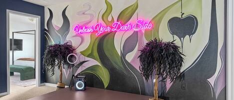 Une pièce avec une grande fresque murale, un bureau avec une radio et deux plantes en pot.