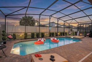 Ein überdachter Pool mit Liegestühlen und aufblasbaren Ringen, umgeben von einer Umzäunung und Häusern.