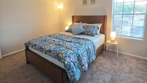 Ein Schlafzimmer mit einem Bett, zwei Wandleuchten, einem Fenster mit Jalousien und zwei gerahmten Bildern an der Wand.