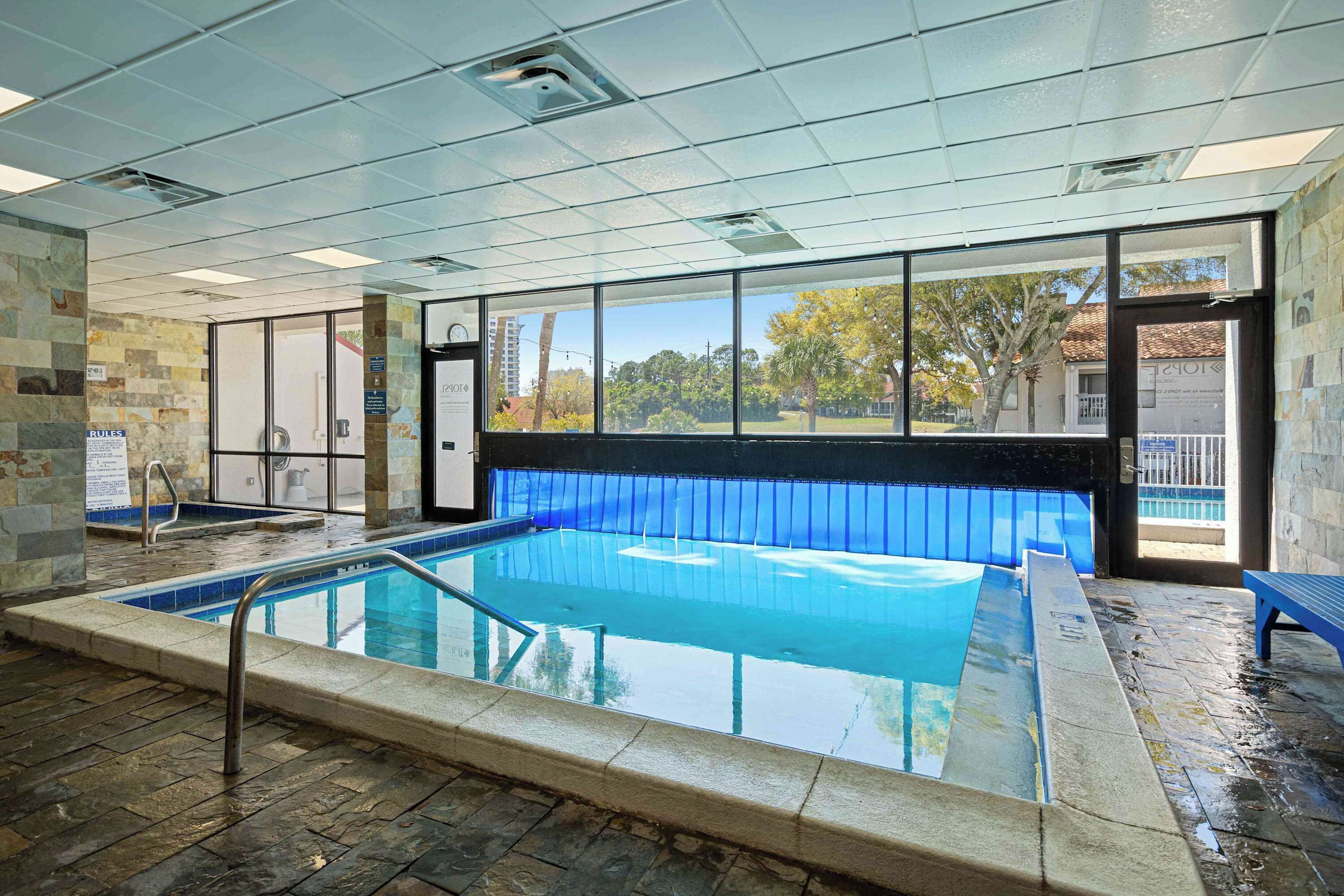 An indoor swimming pool with clear glass walls, a tiled floor, and a view of the outside.