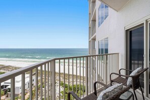 A balcony with wicker furniture overlooking a beach. - Spacious beachfront condo with gulf views (Miramar Beach)