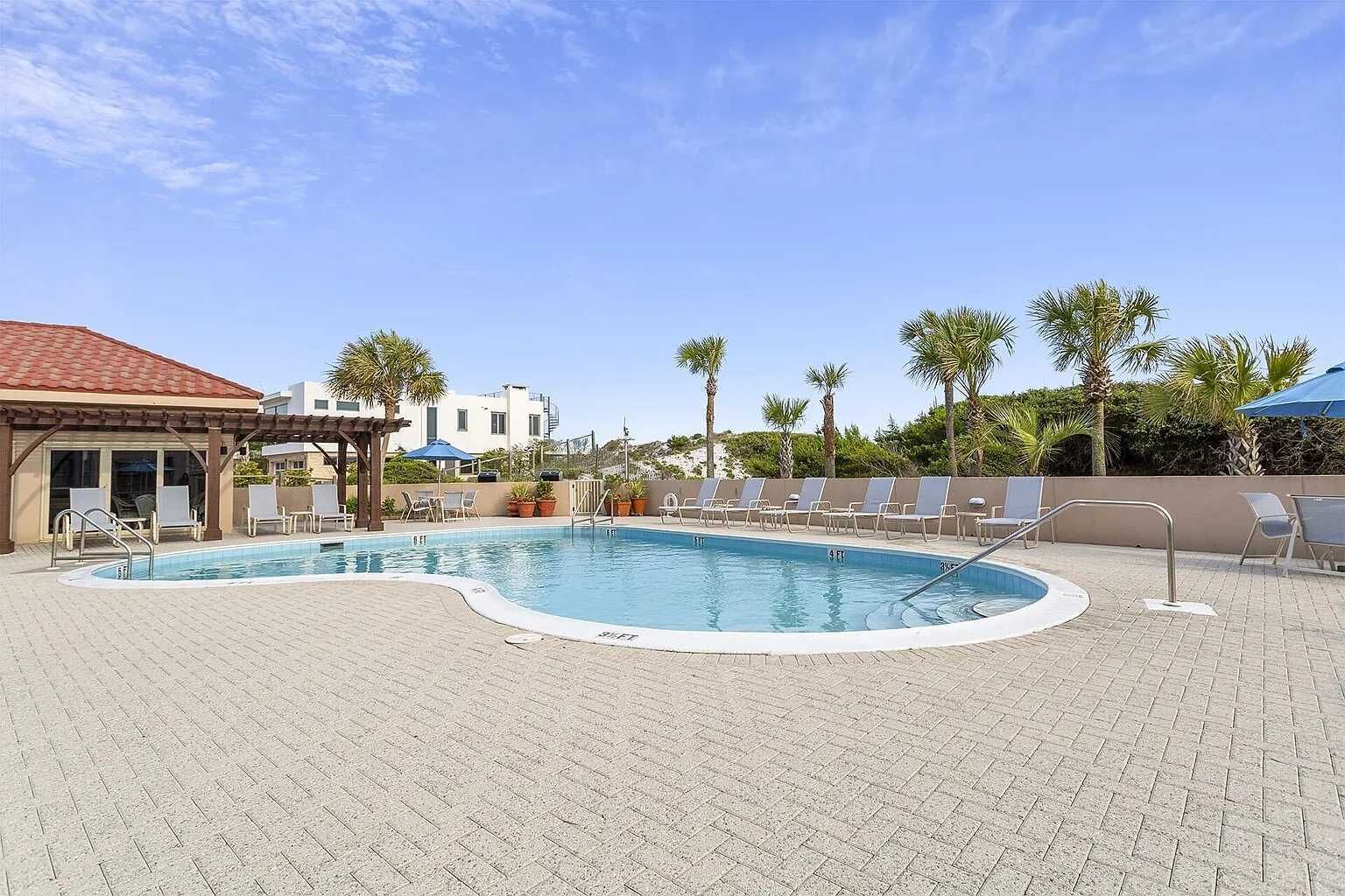 A swimming pool with lounge chairs and a covered seating area.