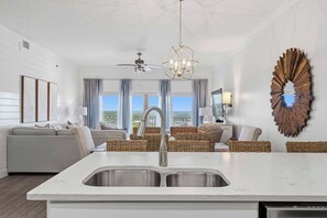 A modern living room with a kitchen island, a ceiling fan, and a large decorative mirror. - Spacious beachfront condo with gulf views (Miramar Beach)