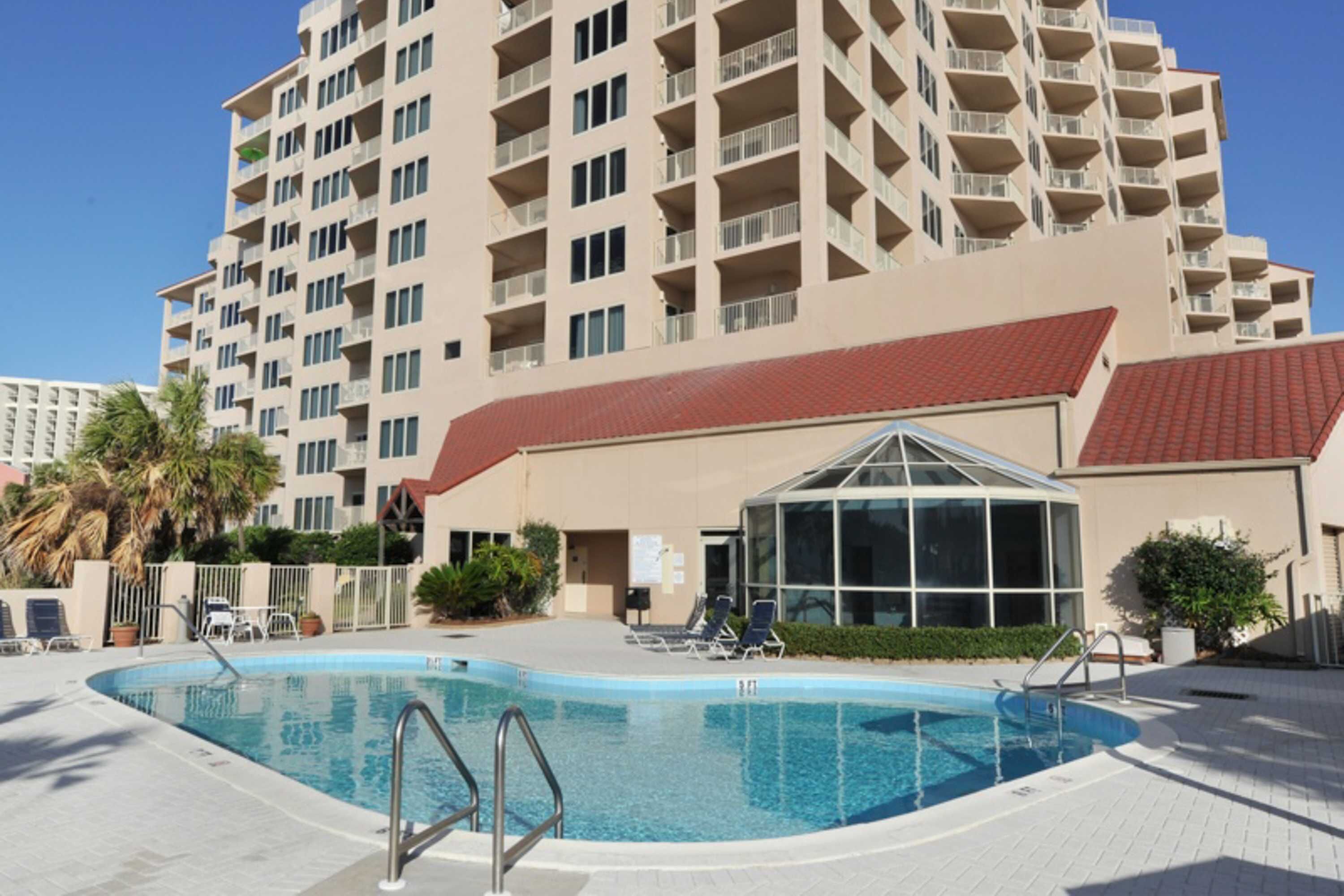 A hotel with a swimming pool, multiple balconies, and a covered area with lounge chairs.