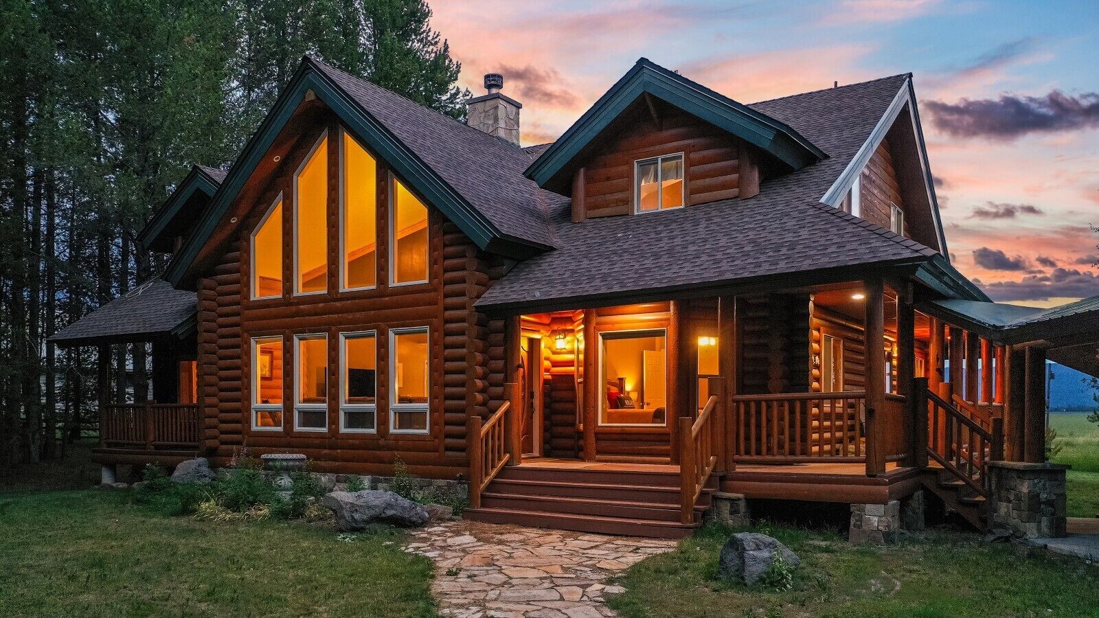 A log cabin with a stone pathway leading to the entrance, large windows, and a porch with a railing.
