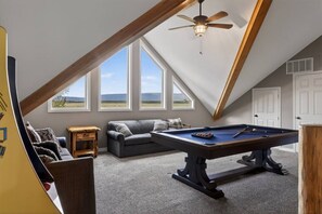 A loft-style room with a pool table, a sofa, and a ceiling fan.