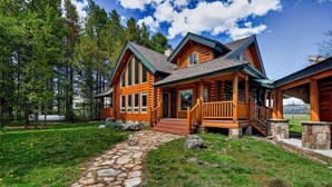 A log cabin with a stone pathway leading to the entrance, surrounded by a grassy area and trees. - Golf Course Cabin | Sleeps 16, Hot Tub, Game Room, Golf, 25min to YSNP (Island Park)