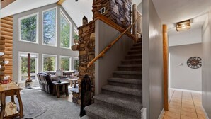 A spacious living area with a stone staircase, large windows, and a cozy seating area. - Golf Course Cabin | Sleeps 16, Hot Tub, Game Room, Golf, 25min to YSNP (Island Park)