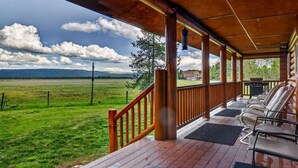 A covered porch with a view of a grassy field and mountains. - Golf Course Cabin | Sleeps 16, Hot Tub, Game Room, Golf, 25min to YSNP (Island Park)