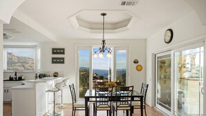 Uma cozinha moderna com ilha central, sala de jantar com mesa e cadeiras, e uma grande porta de vidro deslizante que dá para uma varanda.