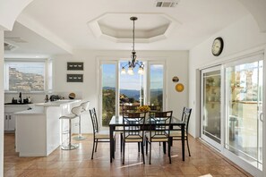 Eine moderne Küche mit einer zentralen Kochinsel, einem Essbereich mit Tisch und Stühlen sowie einer großen Schiebeglastür, die auf einen Balkon führt.