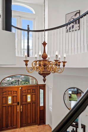 Eine prächtige Treppe mit einem Chandelier, Holztüren mit Buntglas und ein Blick durch ein Fenster.