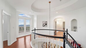 Um interior espaçoso com uma escadaria imponente, paredes brancas e vista através de uma grande janela.