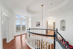 Ein großzügiger Innenraum mit einer imposanten Treppe, weißen Wänden und Blick durch ein großes Fenster.