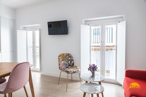 Ein modernes Wohnzimmer mit einem Flachbildfernseher, einem gemusterten Sessel, einem roten Sofa und einem Esstisch.