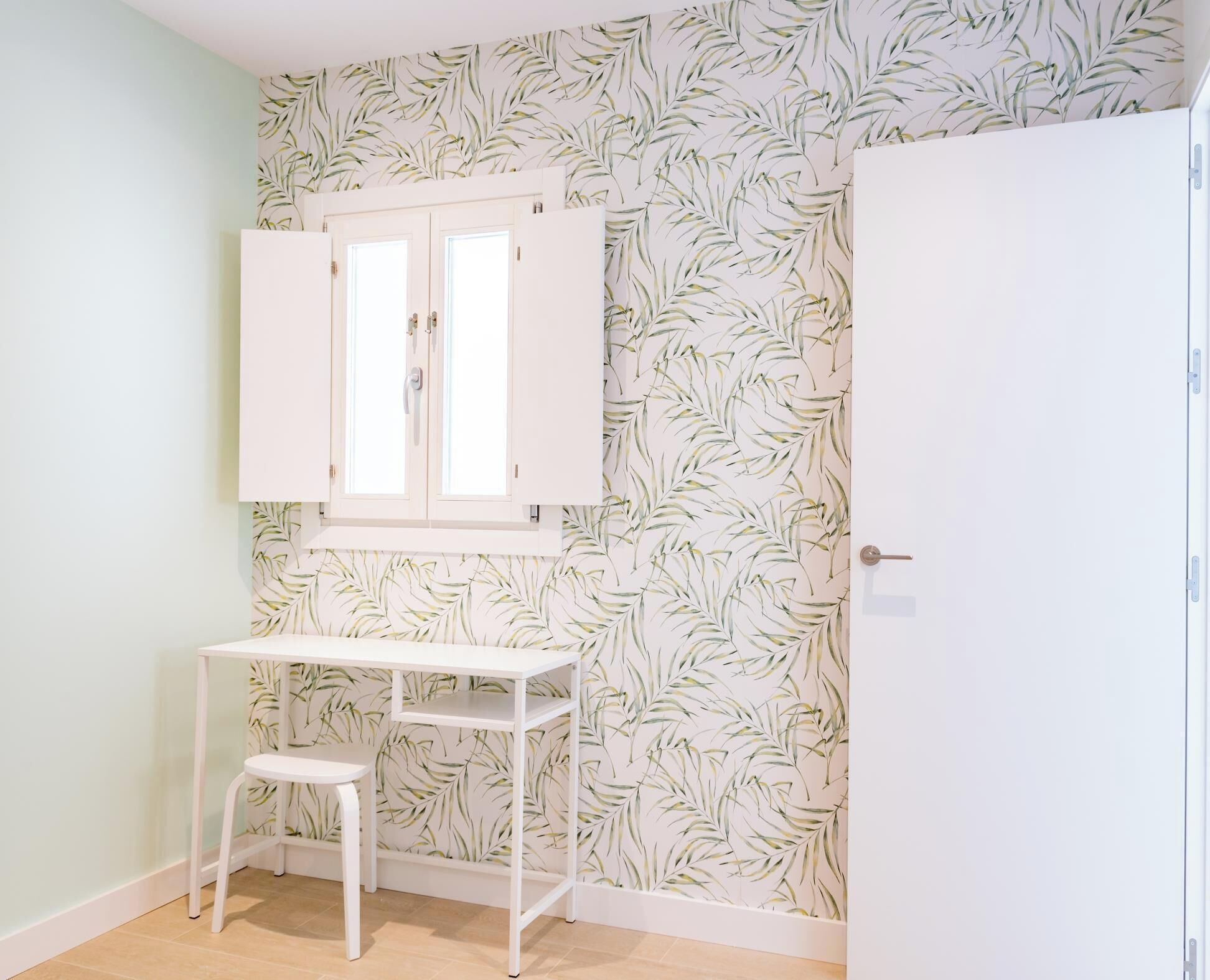 Une pièce avec un bureau blanc, un petit tabouret, une armoire et une porte.