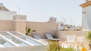 Una terrazza sul tetto con poltrone, ringhiera in vetro e piante in vaso.