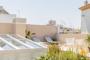 Eine Dachterrasse mit Liegestühlen, einer Glasbrüstung und Pflanzen in Töpfen.