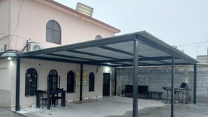 A covered outdoor area with a building in the background, a table, chairs, and a grill. - Casa Cactus (Linares)