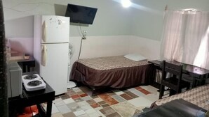 A small, compact room with a bed, a desk, a refrigerator, a stove, and a ceiling fan. - Casa Cactus (Linares)