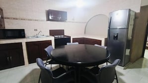 A kitchen with a round table, chairs, a microwave, cabinets, and a refrigerator. - Casa Cactus (Linares)