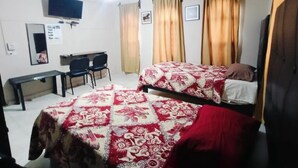 A room with two beds, a desk, a chair, a TV, and curtains.