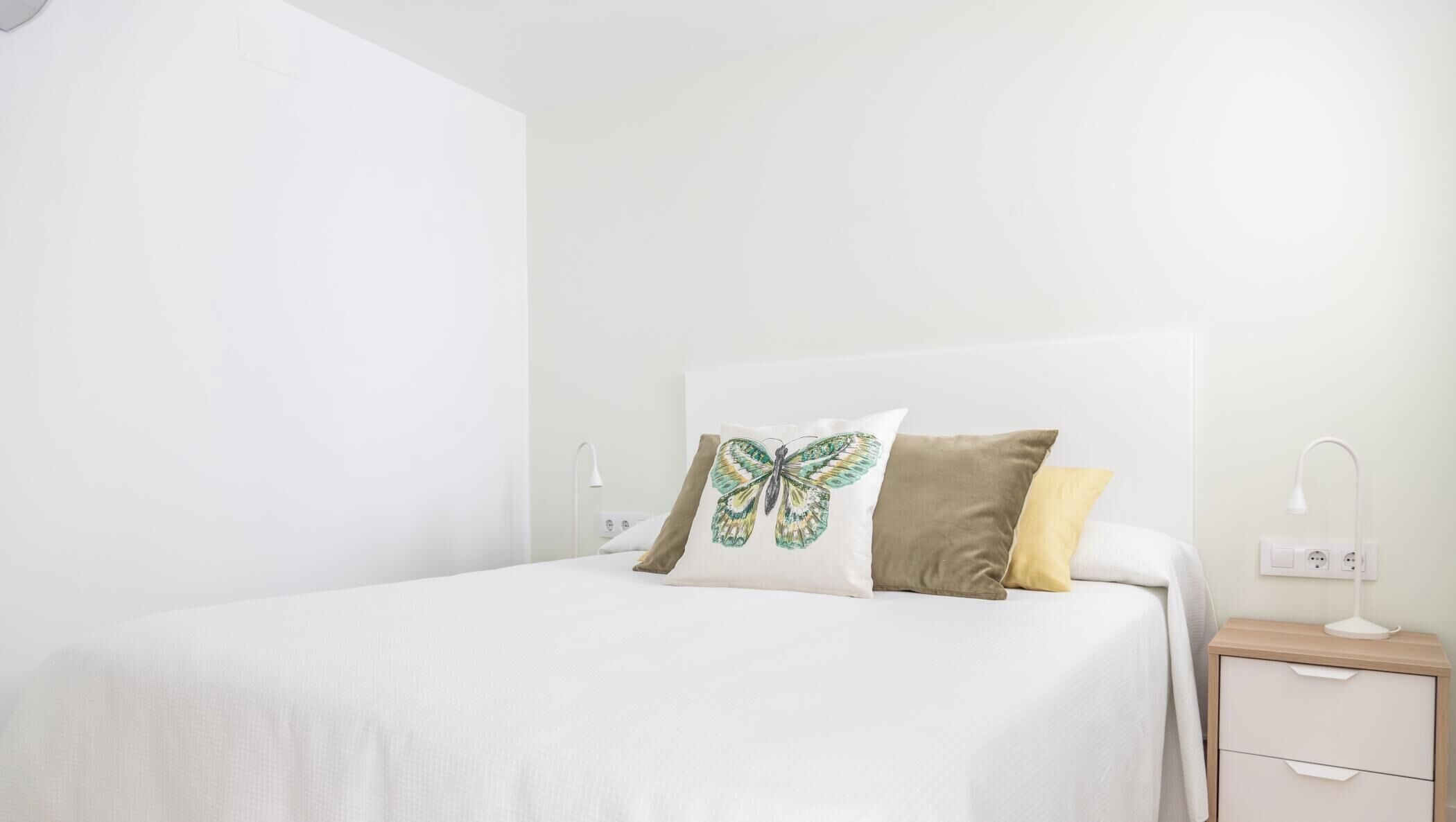 Een slaapkamer met een bed, kussens, een nachtkastje en een lamp.