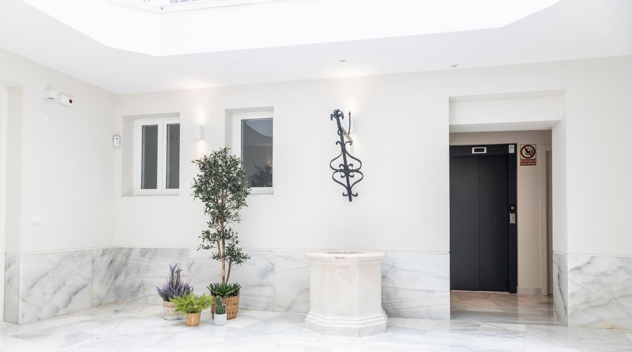 A modern interior with a marble floor, a central column, and potted plants.
