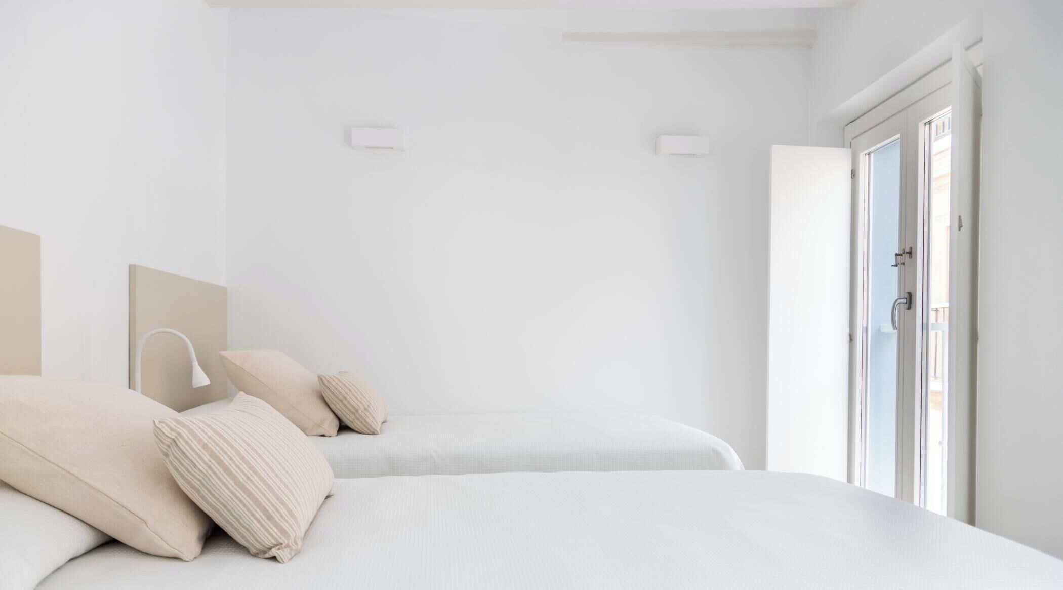 A minimalist bedroom with two beds, a bedside lamp, and a door leading to a balcony.