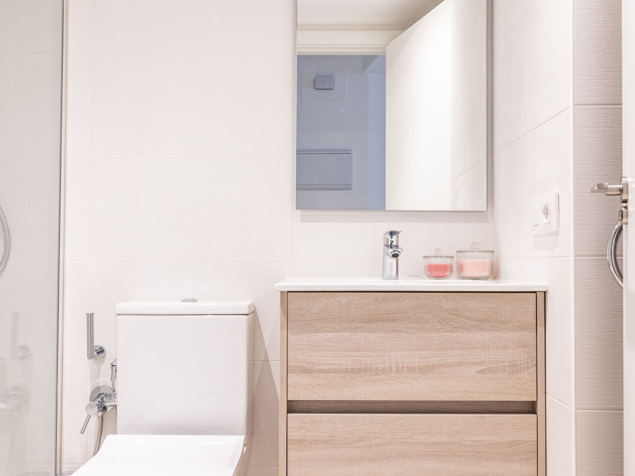 A modern bathroom with a toilet, a shower, a sink with a mirror, and a cabinet.