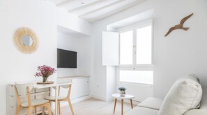 Ein heller, weißer Raum mit Esstisch, Stühlen, Fernseher, Fenster und einer an der Wand befestigten Vogel-Skulptur.