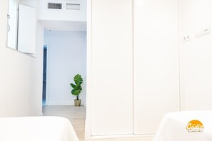Ein moderner, minimalistischer Raum mit einem weißen Schrank, einer Topfpflanze und einer sichtbaren Tür zu einem anderen Zimmer.