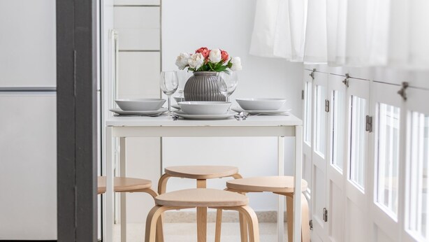 Une cuisine moderne avec des meubles blancs, une table à manger dressée avec des assiettes, des verres et un vase de fleurs.