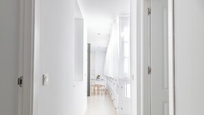 Un couloir lumineux, aux murs blancs, qui mène à une salle à manger avec une table et des chaises.