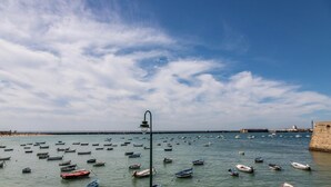 Un paysage côtier avec de nombreux bateaux ancrés dans des eaux calmes, un ciel dégagé et une structure en pierre visible au loin.