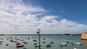 Eine Küstenlandschaft mit zahlreichen kleinen Booten auf ruhigem Wasser, einem klaren Himmel und einer weit entfernten Befestigung.