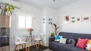 A modern living room with a grey sofa, white chairs, a glass table, and a potted plant. - Atico Catedral by Cadiz Time (Cádiz)