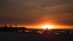 A beach scene with people, a sunset, and a distant building. - Atico Catedral by Cadiz Time (Cádiz)