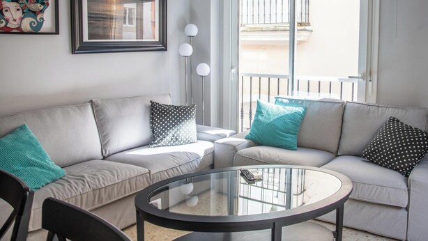 Uma sala de estar moderna com um conjunto de sofá cinza, uma mesa de centro de vidro e uma grande janela com varanda.