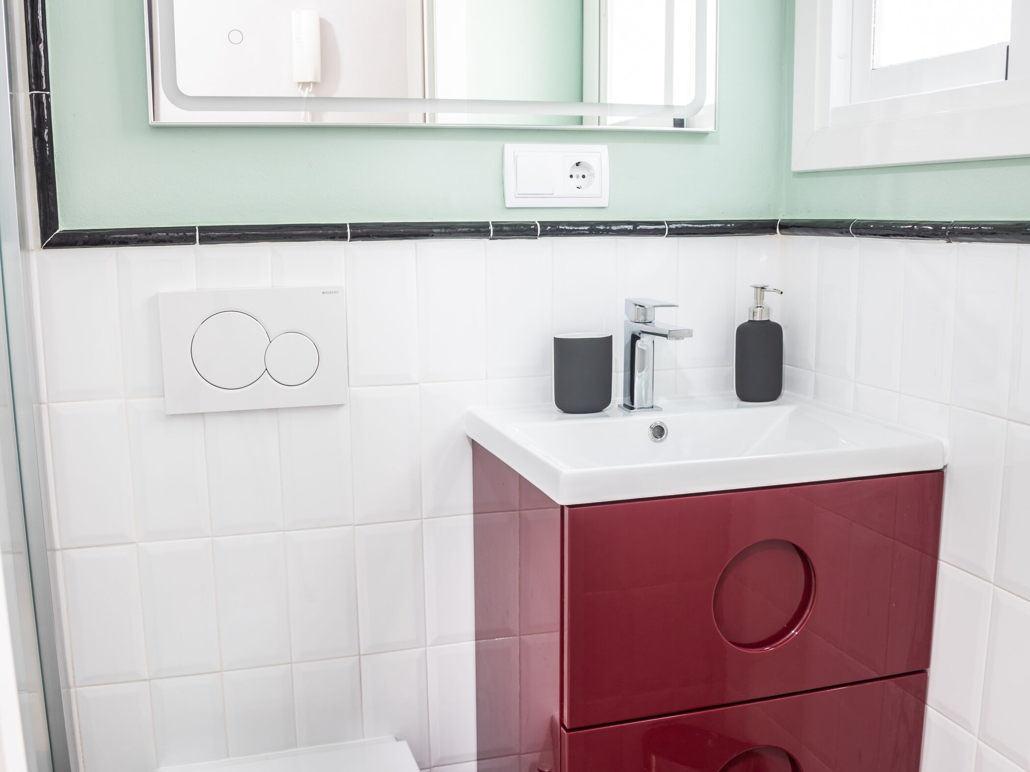Un baño con lavamanos blanco, un espejo, un grifo y un armario rojo.