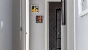 Um corredor com uma porta branca, uma porta de vidro com moldura preta e duas obras de arte na parede.