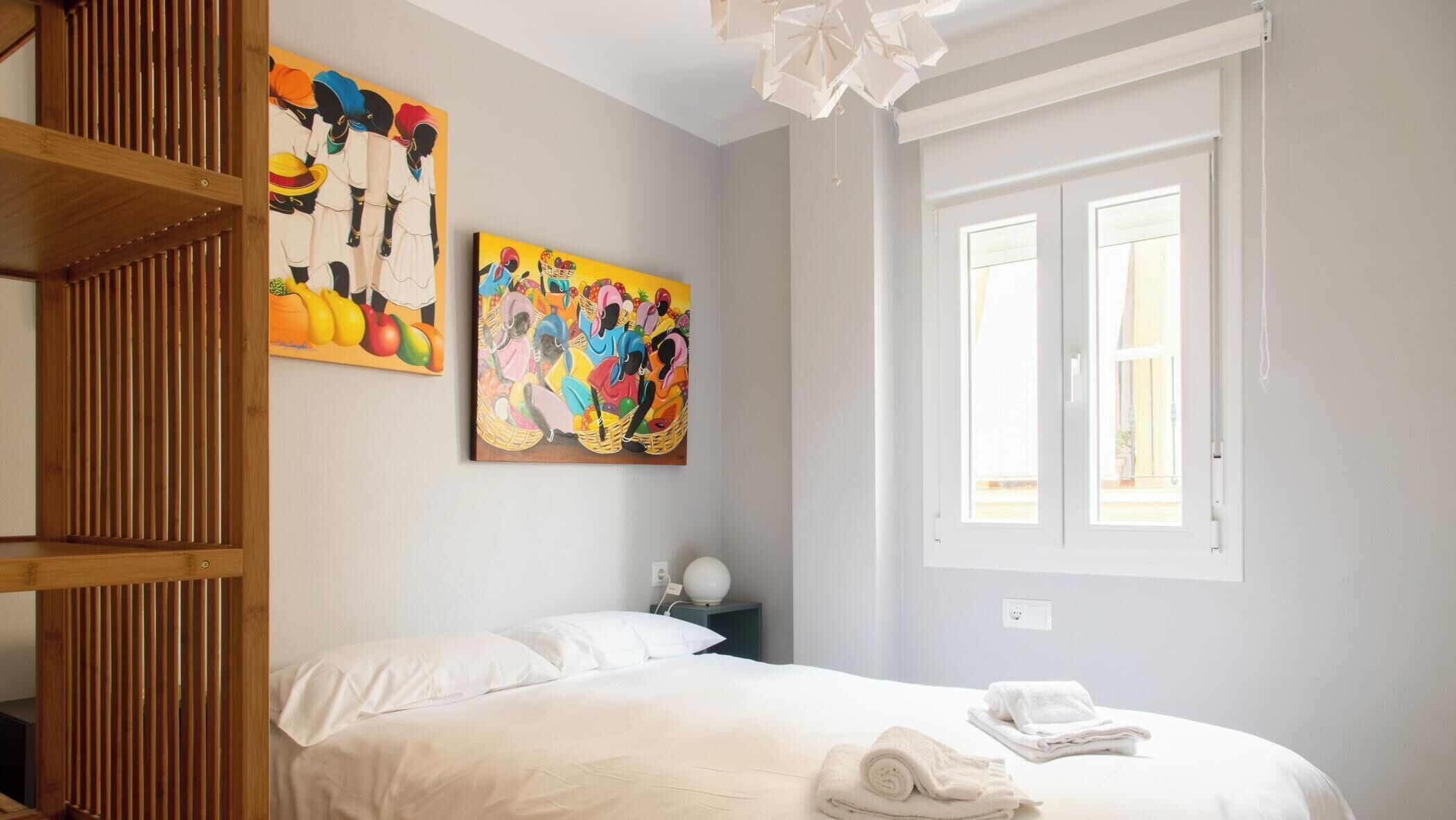 Une chambre à coucher avec un lit, deux tableaux, une fenêtre et une étagère en bois.