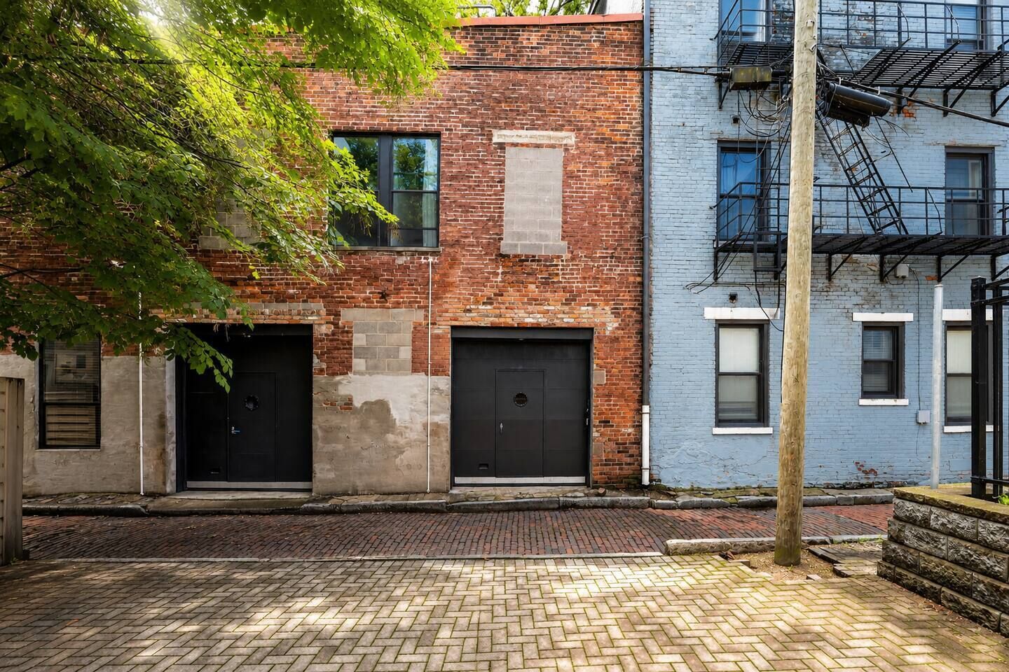 Un bâtiment en briques avec deux portes de garage, un bâtiment bleu avec des fenêtres et une échelle de secours.
