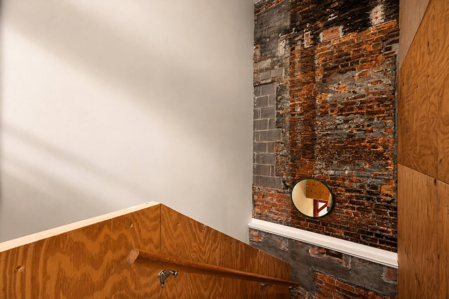 A wooden staircase with a mirror reflecting a brick wall.