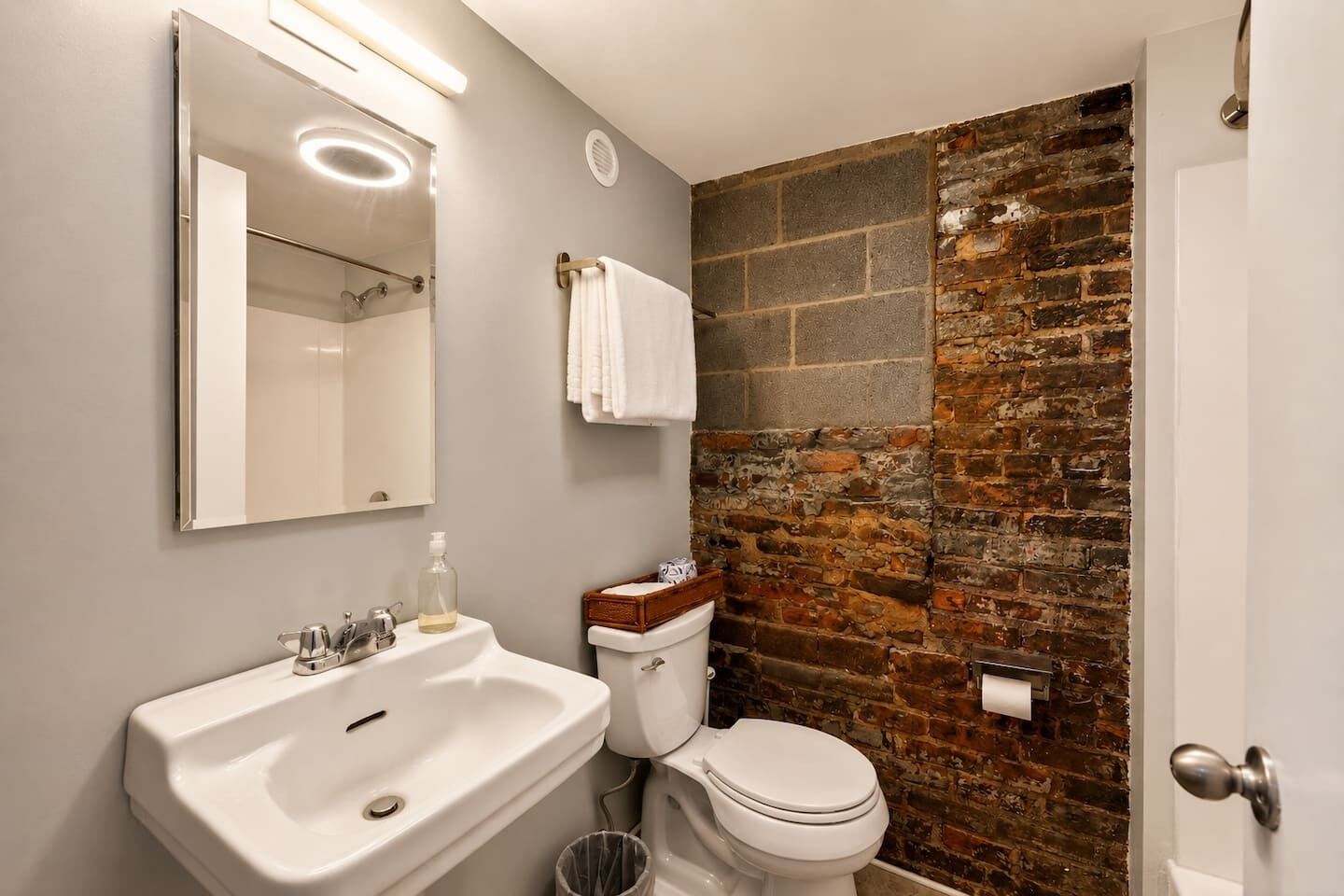 Une salle de bain avec un lavabo blanc, un miroir, des toilettes et un mur en briques.
