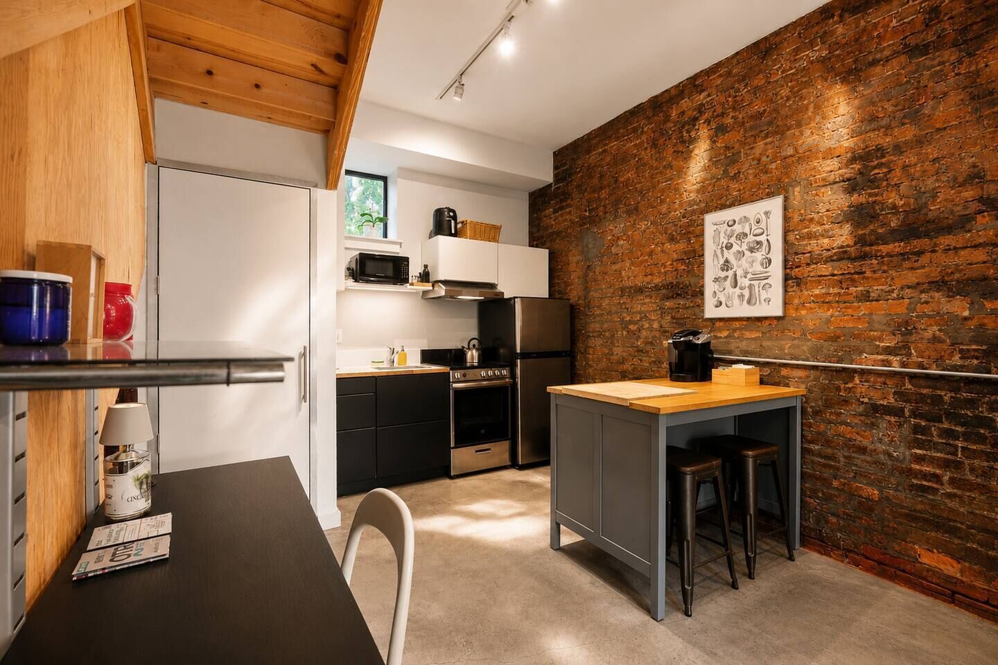 A compact kitchen with a brick wall, a wooden ceiling, and a small island with stools.