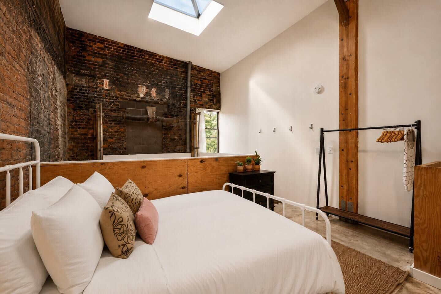 A bedroom with a skylight, a brick wall, a wooden bed, and a small dresser.