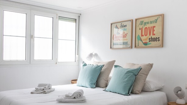 Un dormitorio con cama, almohadas, una mesita de noche, lámpara y dos cuadros en la pared.